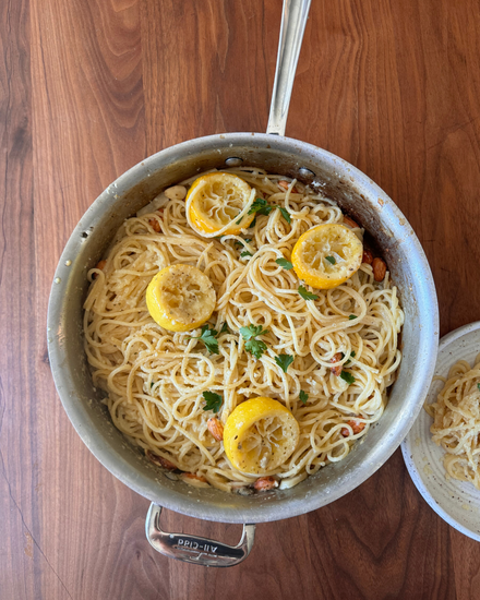 A skillet of spaghetti pasta garnished with lemon slices and herbs.