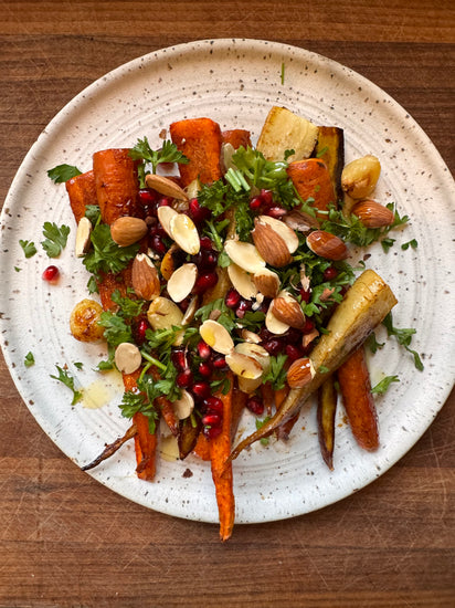 A plate of roasted carrots and parsnips topped with almonds, pomegranate seeds, and fresh herbs.